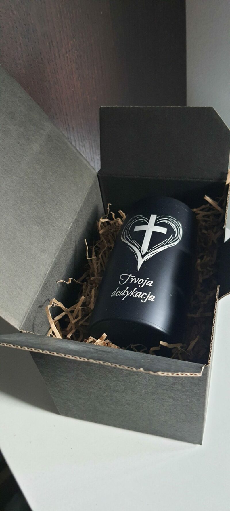 a black cylindrical container with a cross on it inside of a box